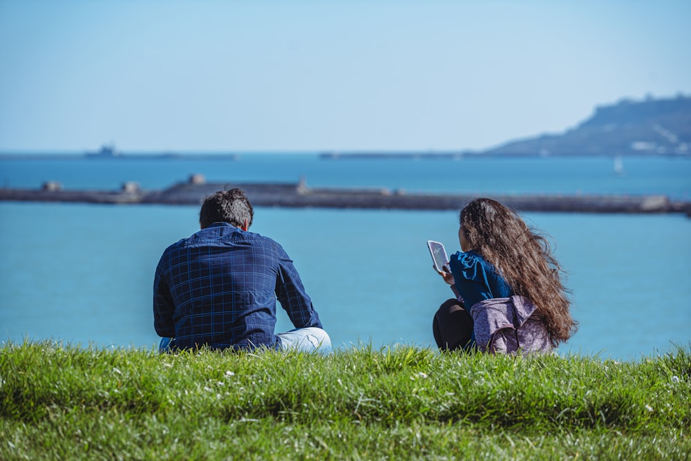 a man and a woman sitting on the grass looking at a cell phone