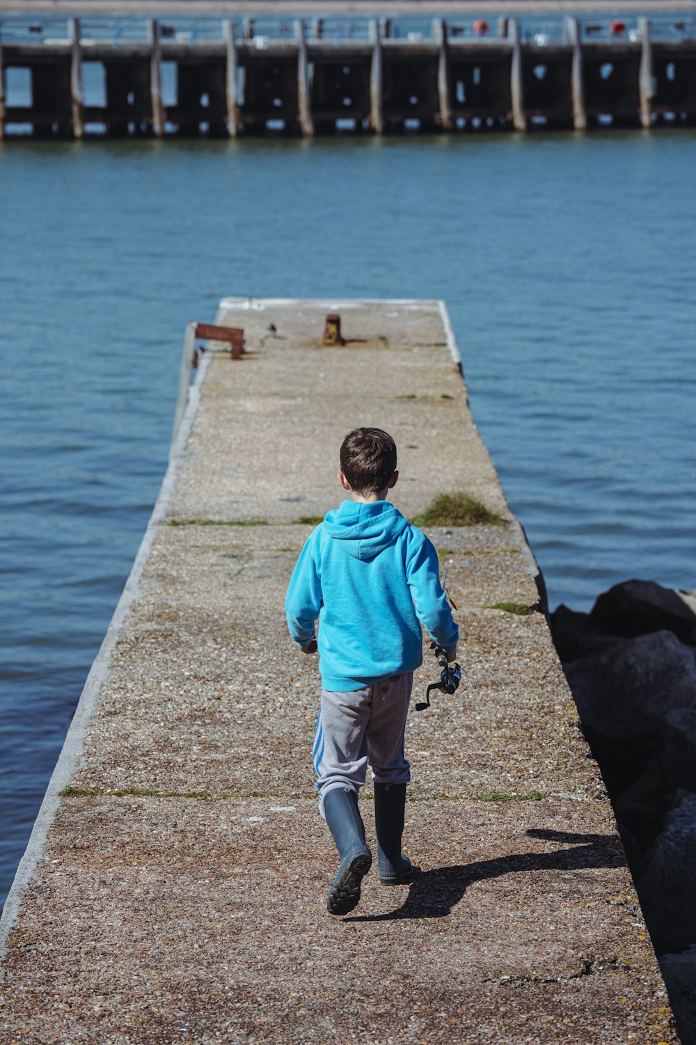 a young boy walking along a pier next to a body of water