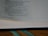 A close-up view of an open book, showing text on a page. The book is lying flat with a visible binding, and lines of text are seen clearly on the page. There is a ribbon bookmark with two green strands visible at the bottom of the image.