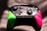 A video game controller featuring a black central section with intricate designs and buttons, flanked by vibrant green and pink grips. It is illuminated dramatically with light and shadow creating a dynamic texture across the surface.