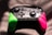 A video game controller featuring a black central section with intricate designs and buttons, flanked by vibrant green and pink grips. It is illuminated dramatically with light and shadow creating a dynamic texture across the surface.