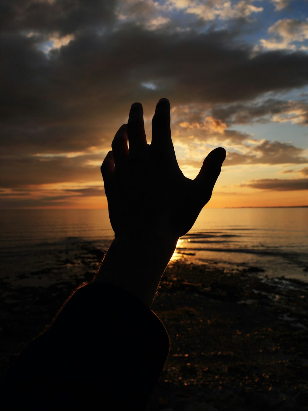 a person holding their hand up in front of a sunset