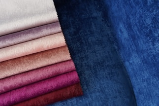 Various shades of fabric are displayed, ranging from pale white and beige to rich purple and deep blue. The fabrics have a velvety texture, capturing light and creating a soft, luxurious appearance.
