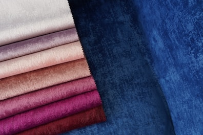 Various shades of fabric are displayed, ranging from pale white and beige to rich purple and deep blue. The fabrics have a velvety texture, capturing light and creating a soft, luxurious appearance.