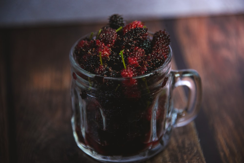 a glass mug filled with raspberries on top of a wooden table