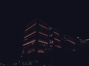 Modern residential building illuminated softly against a dark background with silver lettering.