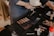 A person is applying makeup using a variety of tools on a black-draped table. There are makeup brushes, an eyeshadow palette, foundation bottle, and other cosmetic items scattered around. The scene suggests a makeup session or preparation for an event.