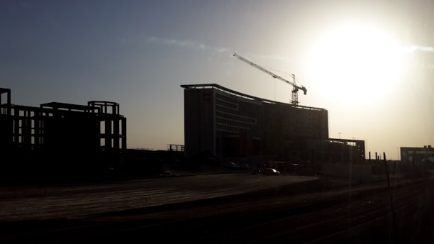 A sleek architectural blueprint overlaying a high-end construction site at sunrise.