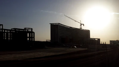 Modern institutional building under construction with cranes and scaffolding at sunrise.