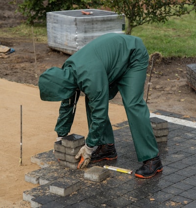 a man in green pants and black shoes working on a brick wall