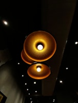 Three large, circular ceiling lights with a warm amber glow are prominently displayed against a dark background. The lights have a textured surface and emit a soft, inviting illumination. Smaller white spotlights are scattered throughout the ceiling, contributing to a cozy ambiance.