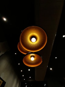 Three large, circular ceiling lights with a warm amber glow are prominently displayed against a dark background. The lights have a textured surface and emit a soft, inviting illumination. Smaller white spotlights are scattered throughout the ceiling, contributing to a cozy ambiance.