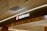 A retail store sign with the brand name 'lululemon' illuminated in white letters on a dark background. The sign includes the brand's recognizable logo, a stylized 'A' in a red circle to the left of the name. The store's interior features modern lighting and design elements with a ceiling composed of recessed lighting and metallic ventilation grates.