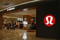 A well-lit retail store featuring a modern and sleek entrance with prominent branding. The interior is visible with displays of clothing and accessories, suggesting an apparel store. The store has a structured layout and several mannequins.