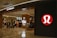 A well-lit retail store featuring a modern and sleek entrance with prominent branding. The interior is visible with displays of clothing and accessories, suggesting an apparel store. The store has a structured layout and several mannequins.