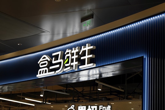 A store entrance with a prominent sign in Chinese characters, backlit by blue neon lights. The sign has a modern design with a clean and sleek appearance. Below the main sign, there is an additional English word 'Fruit', indicating the type of products available in the store.