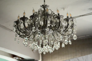 A luxurious, intricate chandelier is hanging from the ceiling, adorned with numerous crystal pendants and ornate metalwork. The chandelier features several bulb sockets shaped like candles, contributing to a classic and elegant appearance. The crystals catch and reflect light, adding a touch of sparkle.