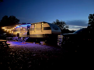 A sleek, modern travel trailer in safety orange parked at a rugged jobsite at dawn.
