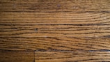 Wooden floor planks with visible grain and texture, featuring some scratches and imperfections.