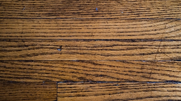 Wooden floor planks with visible grain and texture, featuring some scratches and imperfections.