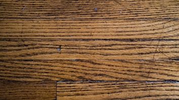Wooden floor planks with visible grain and texture, featuring some scratches and imperfections.