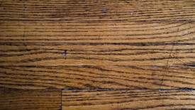 Wooden floor planks with visible grain and texture, featuring some scratches and imperfections.