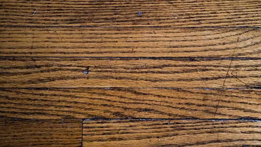 Wooden floor planks with visible grain and texture, featuring some scratches and imperfections.