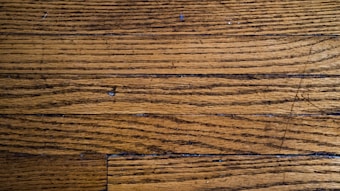 Wooden floor planks with visible grain and texture, featuring some scratches and imperfections.