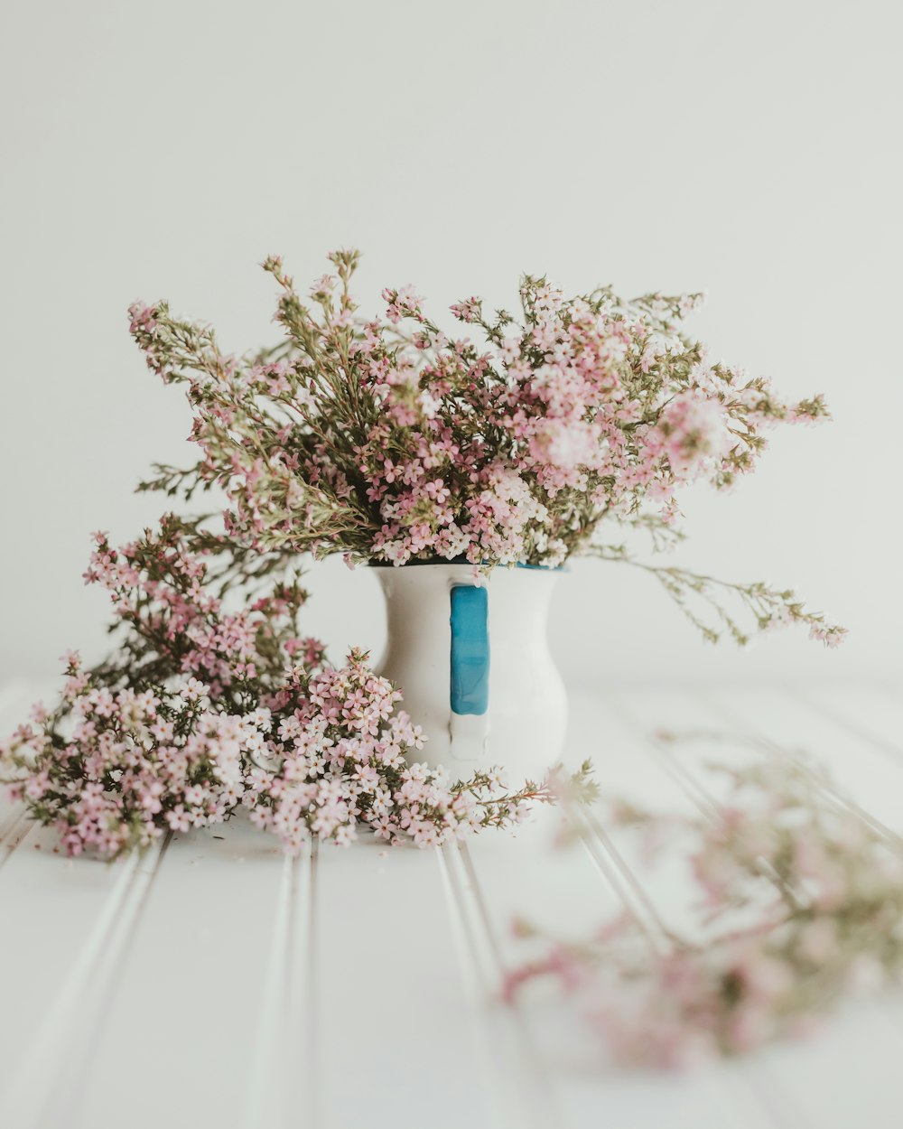 a white vase filled with pink flowers on top of a table