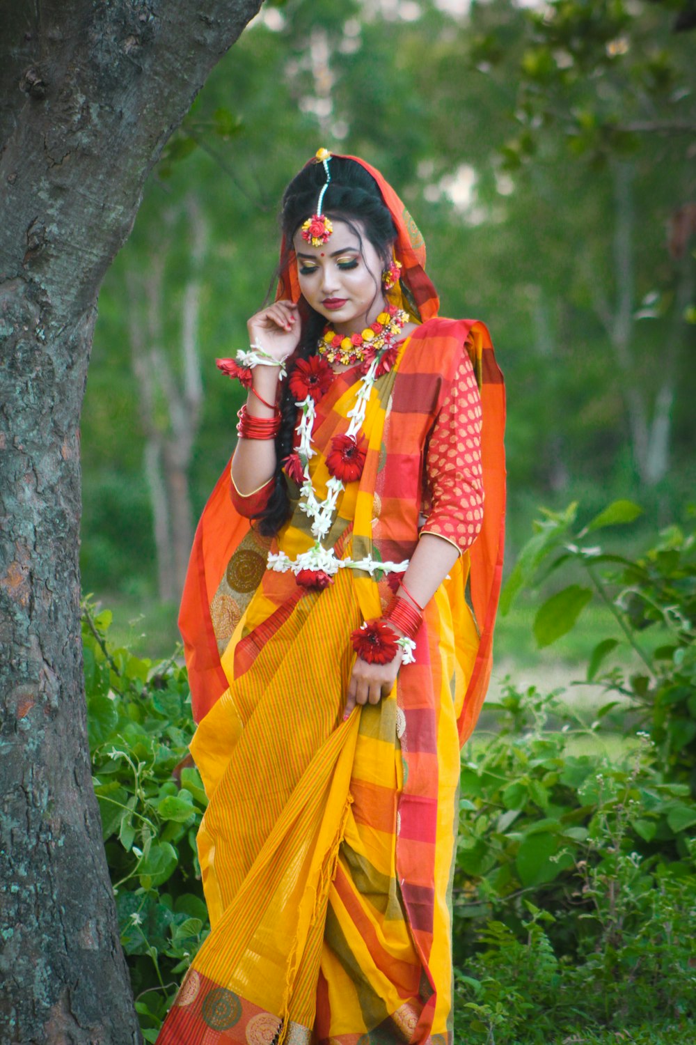 a woman in a yellow and red sari standing next to a tree