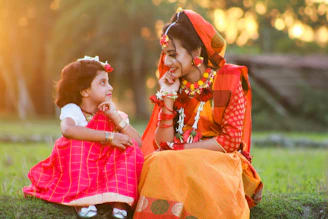 a woman sitting next to a little girl on a lush green field