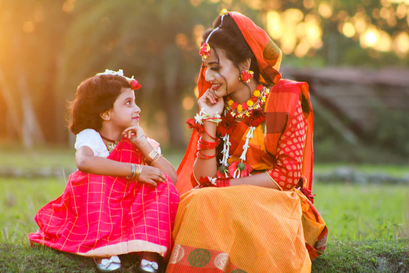 a woman sitting next to a little girl on a lush green field