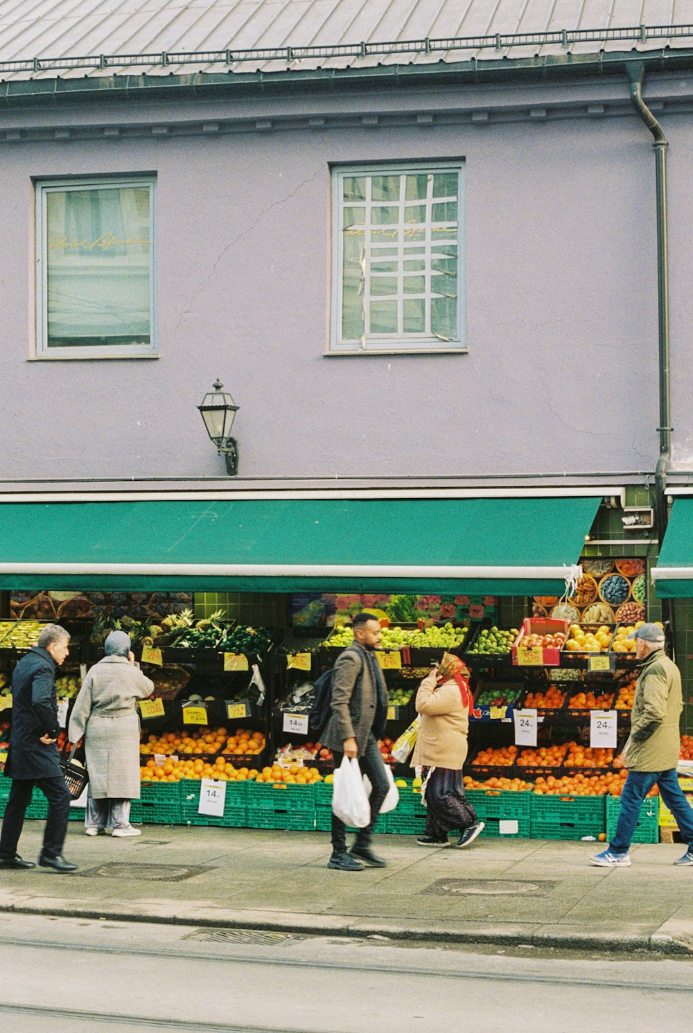 a group of people walking past a fruit stand