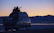 A happy couple standing beside their rented van with a scenic mountain backdrop at sunset.