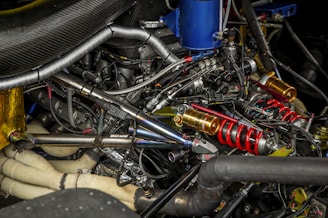 A complex arrangement of mechanical components, including metallic pipes, coils, and various connectors. Prominent red springs and gold-colored cylindrical parts are visible among an intricate web of wires and metal tubing.