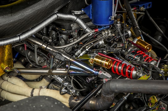 A complex arrangement of mechanical components, including metallic pipes, coils, and various connectors. Prominent red springs and gold-colored cylindrical parts are visible among an intricate web of wires and metal tubing.