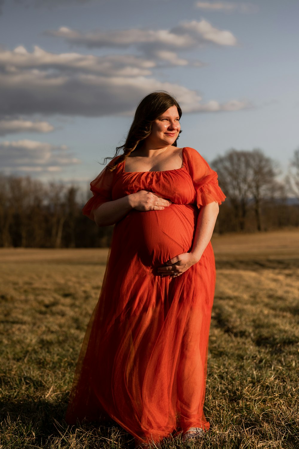 a pregnant woman in an orange dress standing in a field