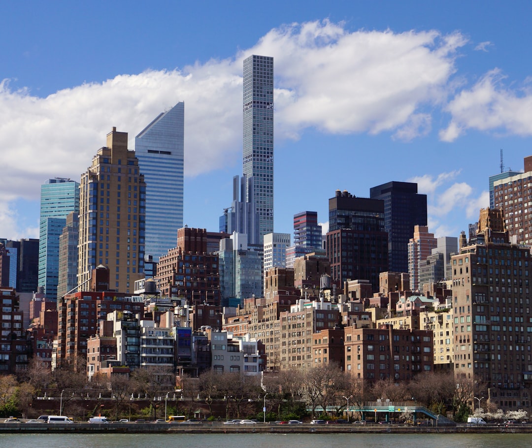 a view of a city with tall buildings and a body of water, Midtown Manhattan view from Roosevelt Island on a sunny spring day.