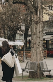A woman carrying a tote bag while walking in a park.