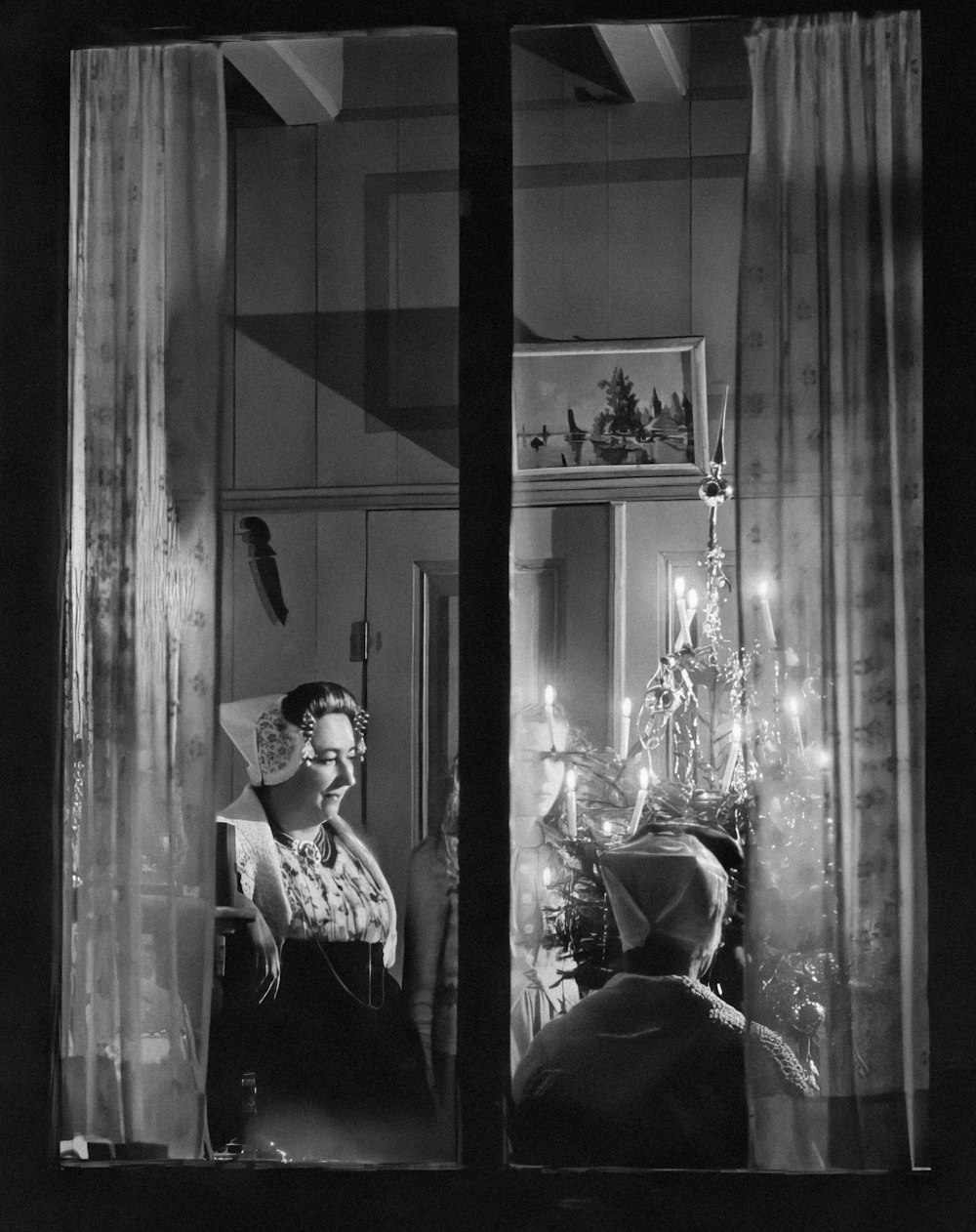 a black and white photo of a woman looking out a window