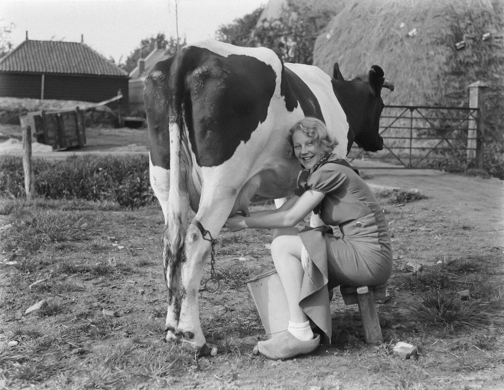 a woman kneeling down to milk a cow