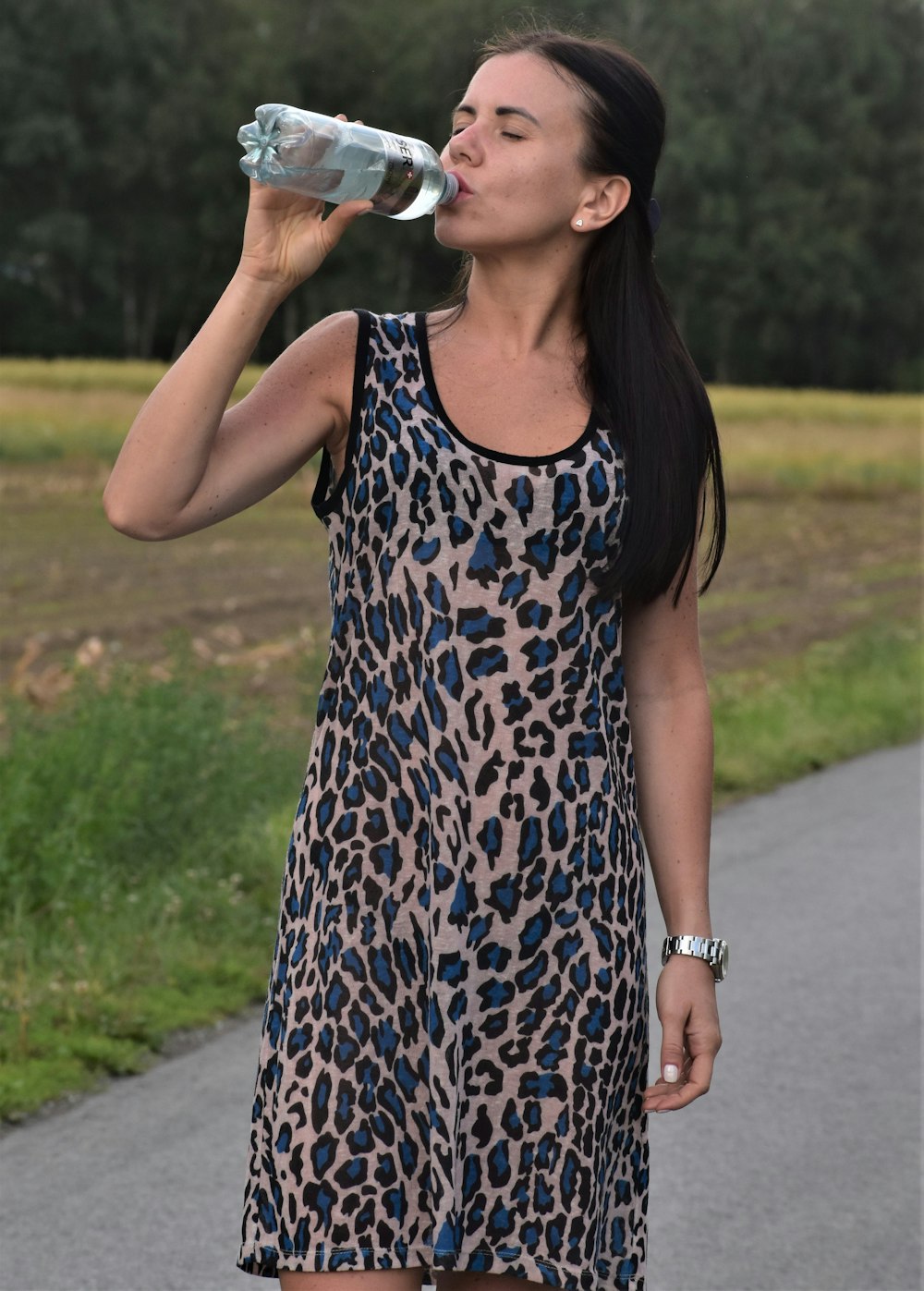 A woman in a leopard print dress drinking from a water bottle