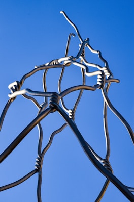 A modern sculpture made of intertwined metal rods reflecting light.