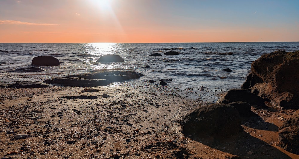 the sun is setting over the ocean with rocks