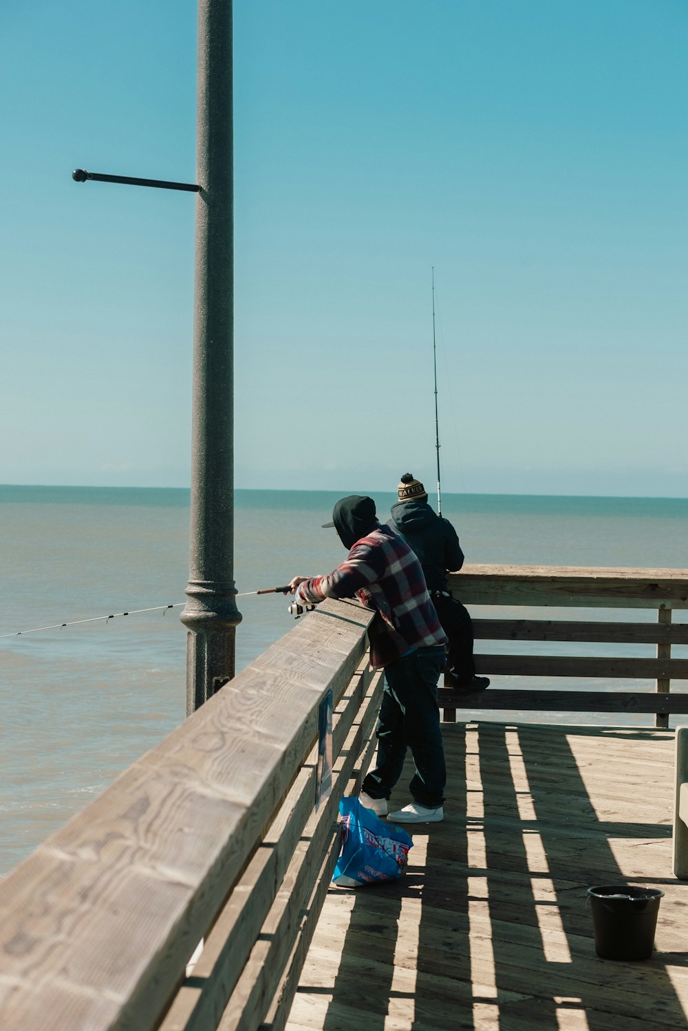 two men fishing on a pier next to the ocean