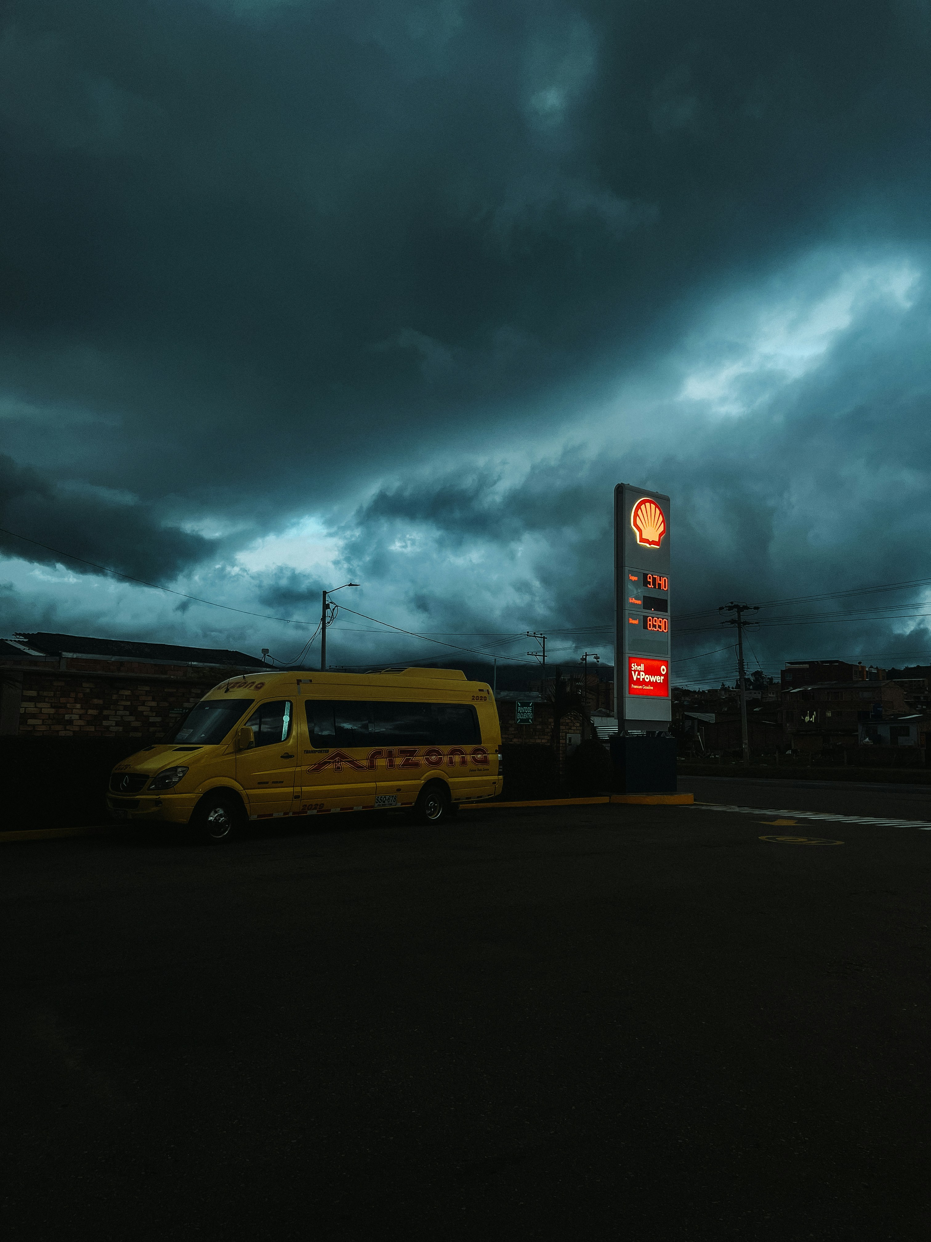 Dark clouds loom over a yellow van and gas station.