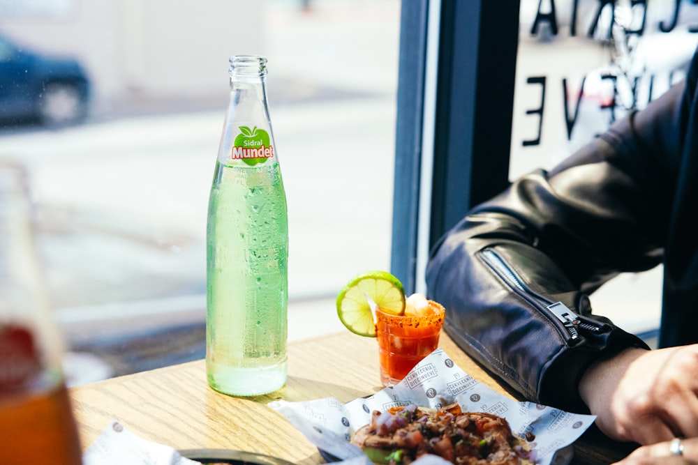 a person sitting at a table with a bottle of soda and a plate of food