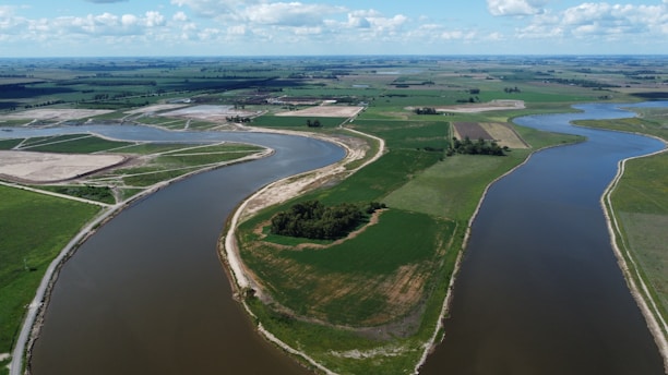 Aerial view of vast Brazilian farmland with green fields and a winding river under a clear sky.