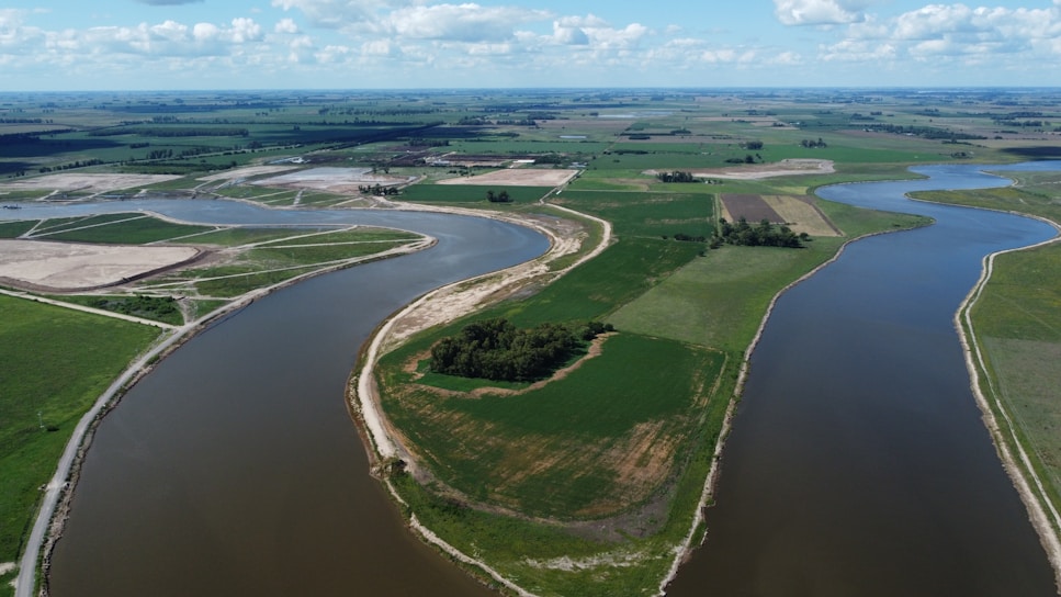 A serene aerial view of green agricultural plots bordered by a winding river under a soft morning light.