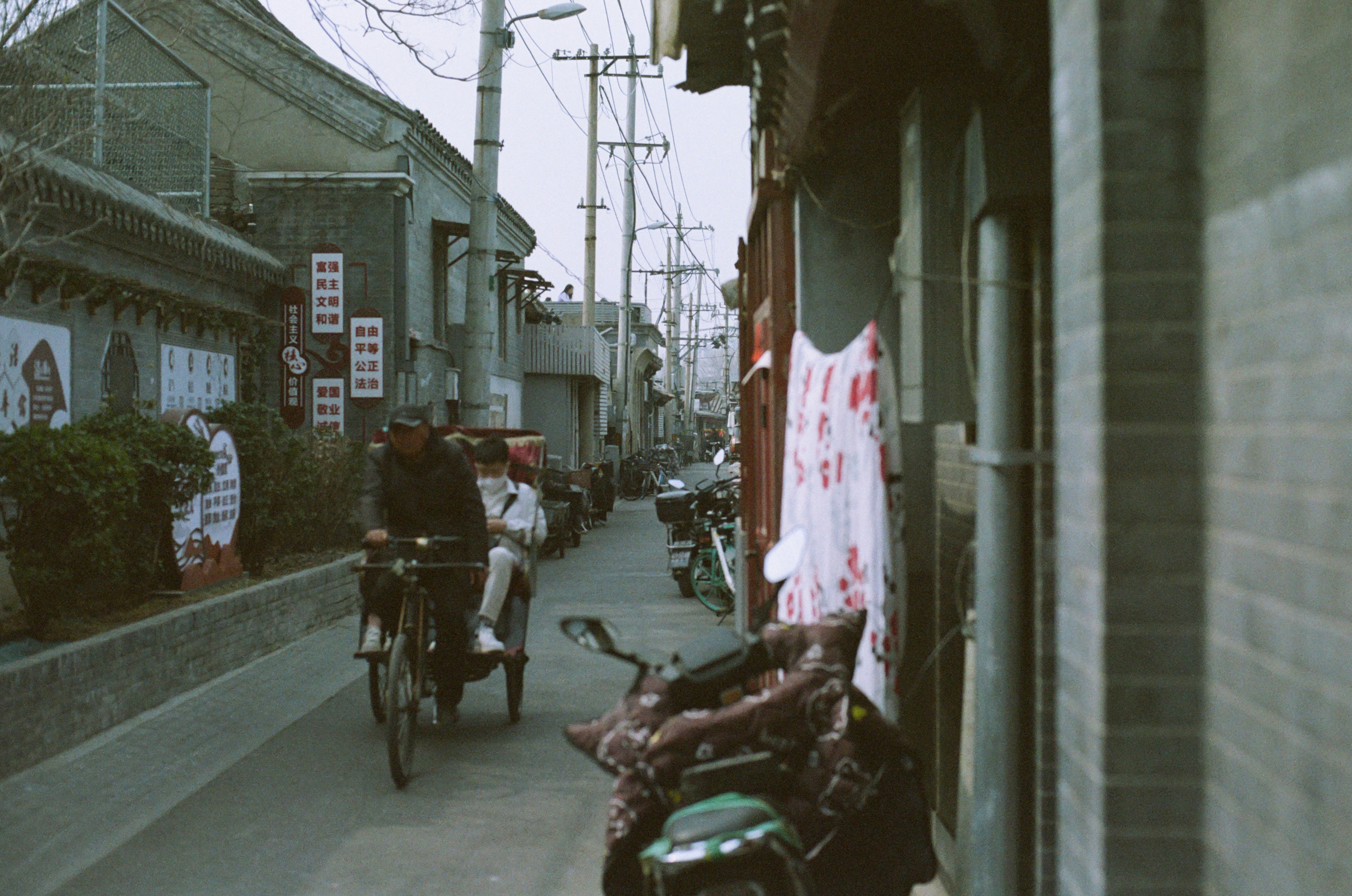 a couple of people riding bikes down a street, There will be special people to take tourists and ride through the alleys in old-fashioned tricycles.